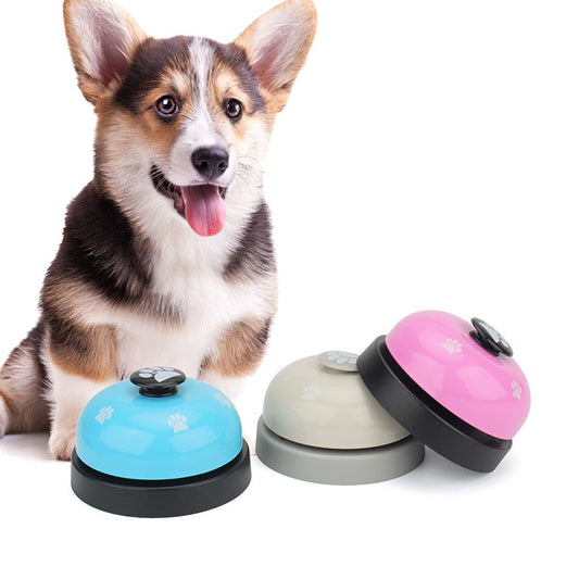 Corgi sitting next to dog potty bells in blue, gray and pink