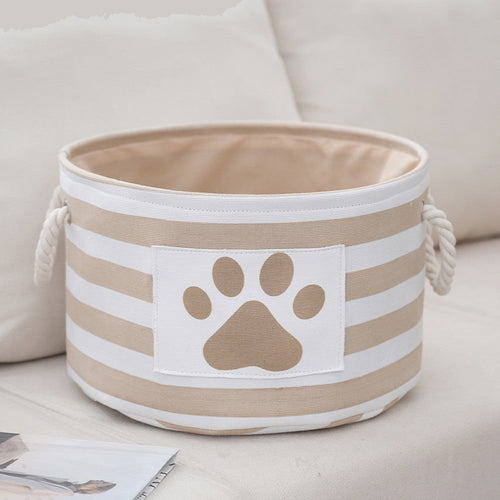 Round striped dog toy basket in beige with a paw print patch and rope handles