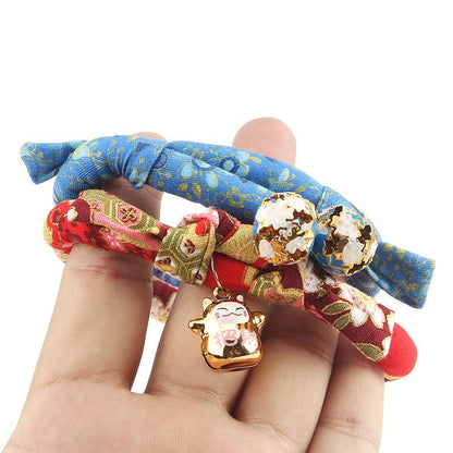 Hand holding kimono cat collars with lucky cat and gold bells