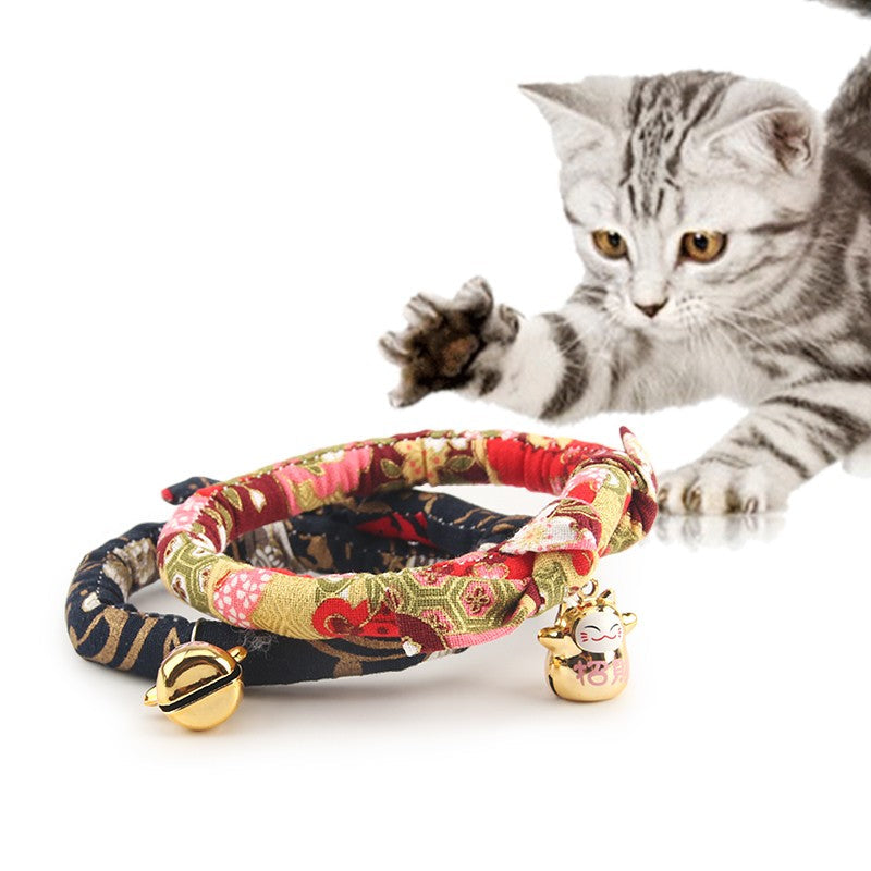 Tabby kitten playing beside kimono cat collars with gold bells