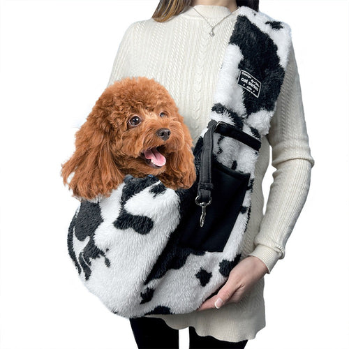 Plush pet carrier bag in black and white cow print worn with a poodle inside